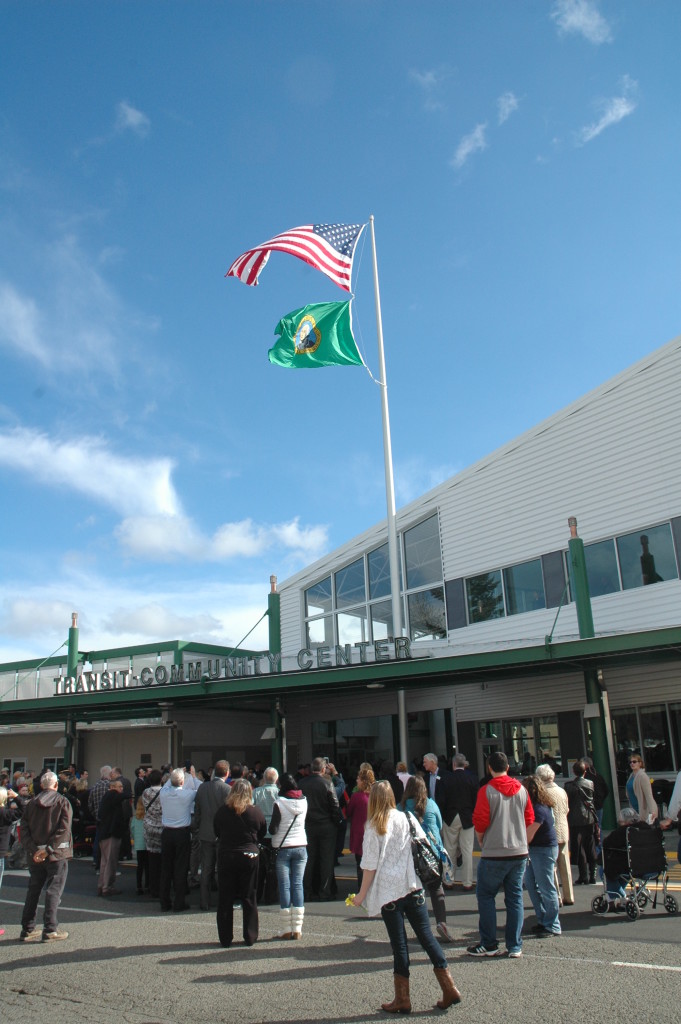 Many community members gather outside on a sunny day at the Transit-Community Center grand opening ceremony to watch the flag being raised. 